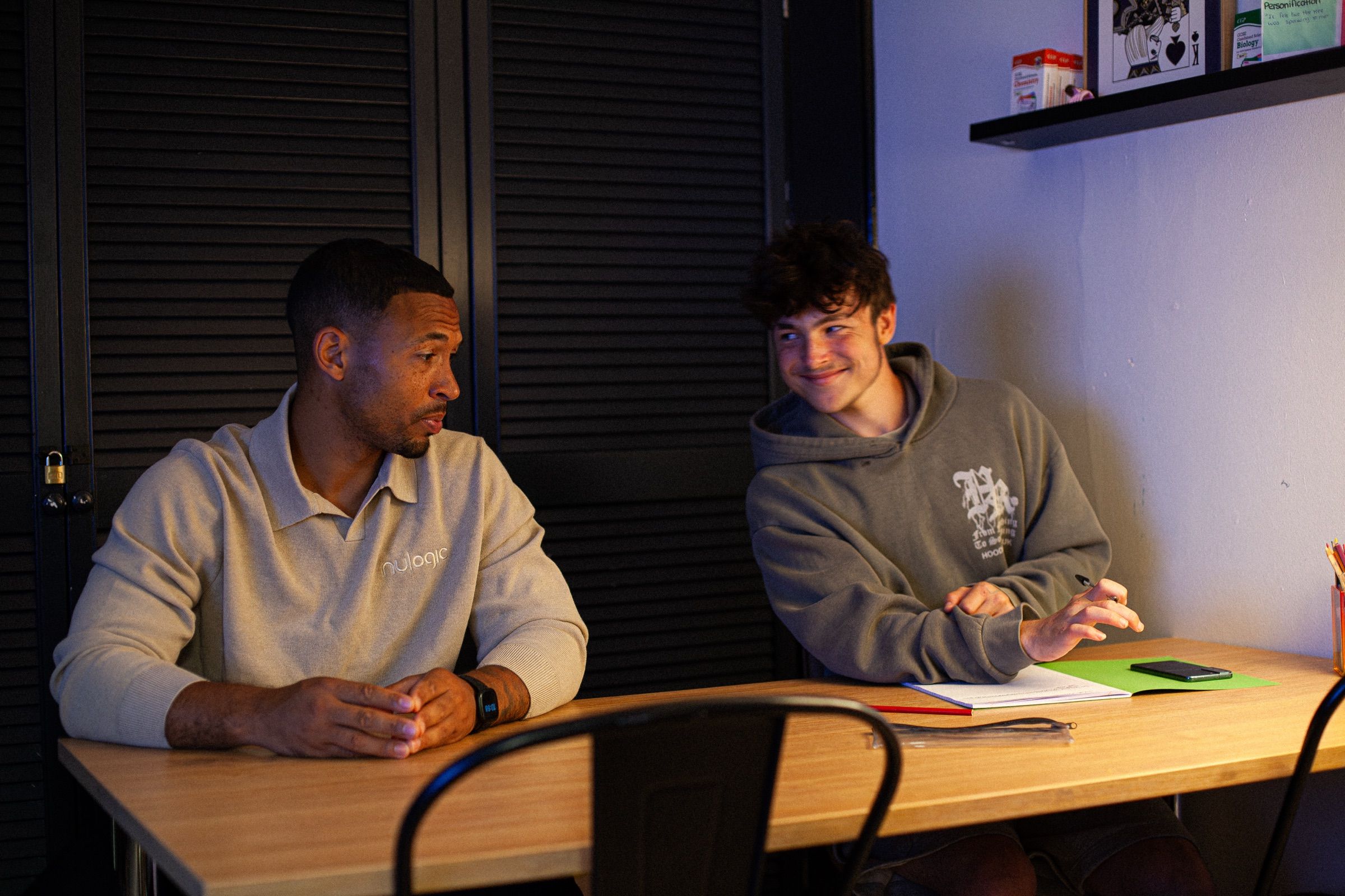 A Nulogic mentor and a teenager talk across a desk, both smiling.