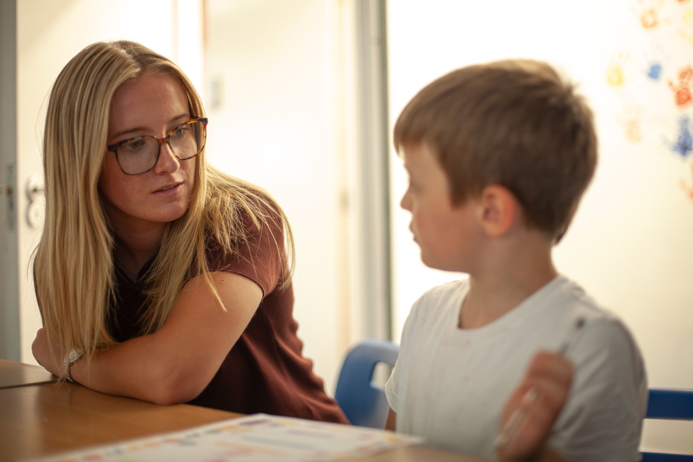 A Nulogic practitioner and a boy talk at a classroom table.